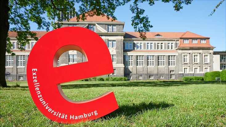 Das rote Exzellenz-E steht auf der Wiese hinter dem Hauptgebäude der UHH